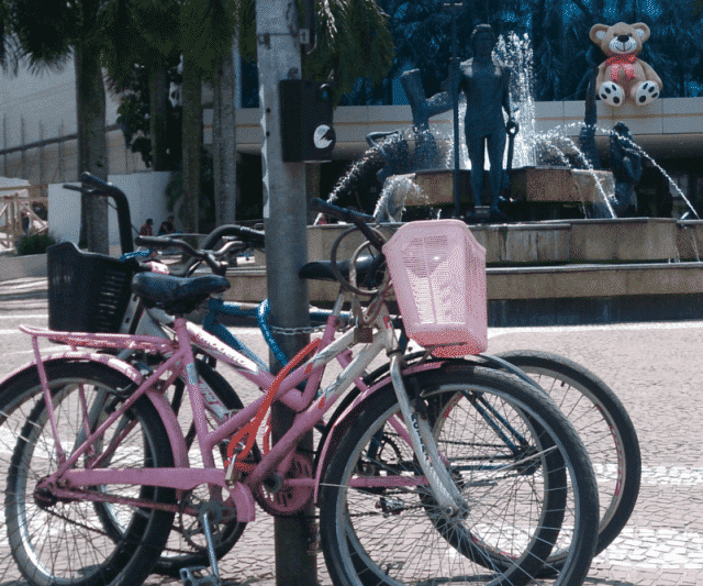 Viver sem carro - Duas bicicletas, uma rosa claro e uma azul, presas a um poste.