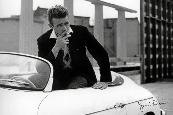 James Dean posa dentro de um carro, enquanto fuma. Antigamente, os carros eram sinal de status, hoje em dia, já é possível contemplar a experiência de viver sem carro.