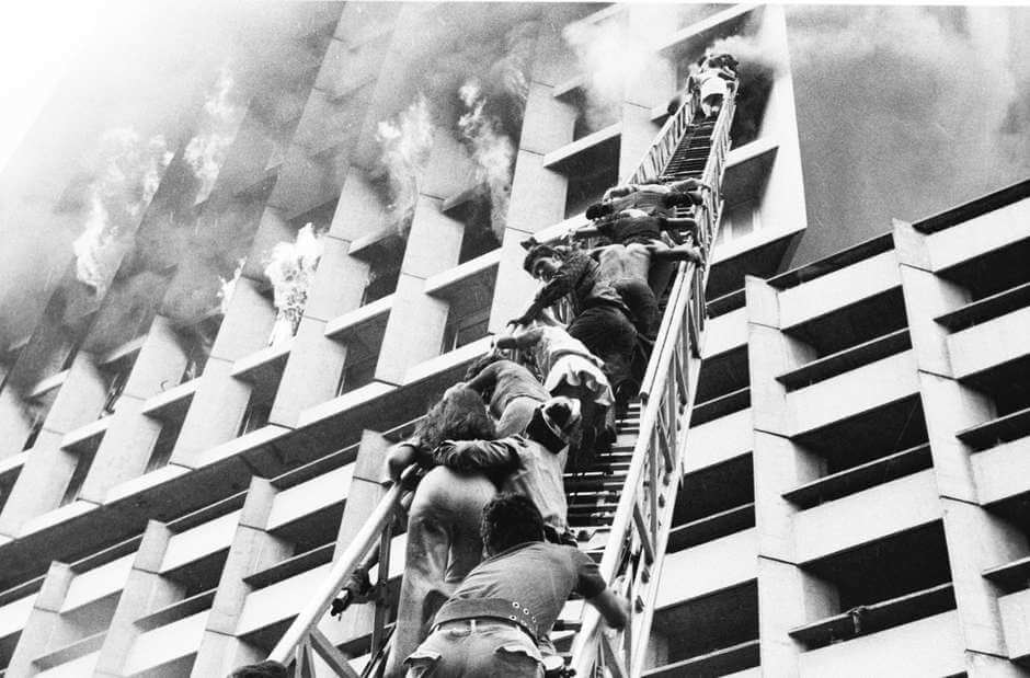 Pessoas sendo salvas por meio dos bombeiros que utilizavam uma grande escada para retirá-las do prédio em chamas.