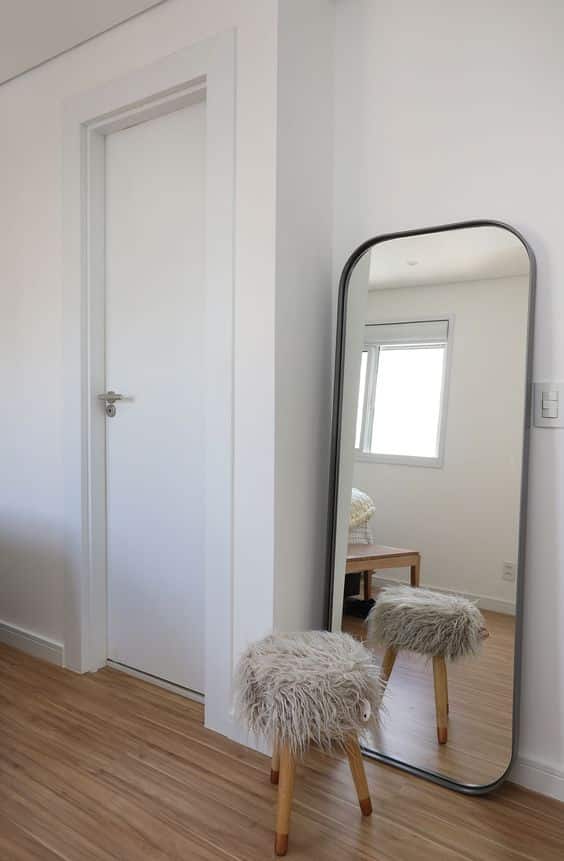 Detalhe de um dormitório com decoração minimalista: um espelho de corpo inteiro reflete uma banqueta.