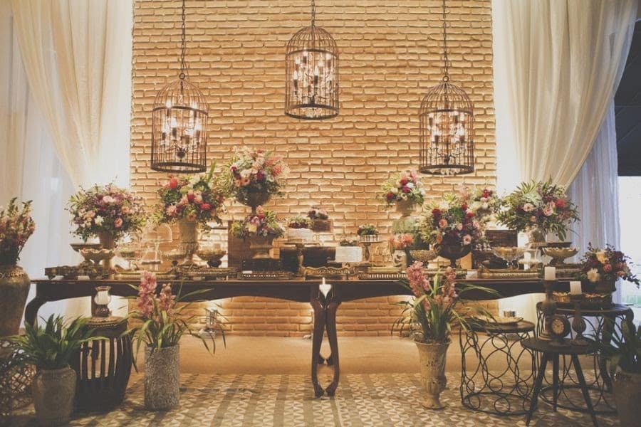 Decoração vintage para casamento com a mesa com madeira escura decorada com lindas flores e iluminação elegante.