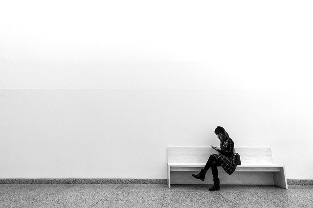 Mulher sentada em um banco num ambiente minimalista, em preto e branco.