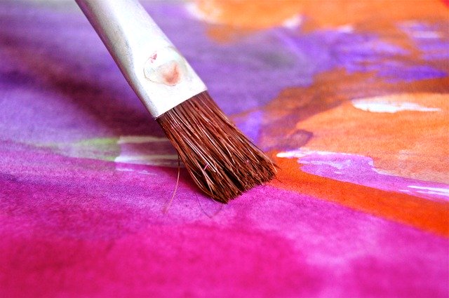 Pincel sendo passado em uma folha colorida com roxo, anil, rosa e laranja.
