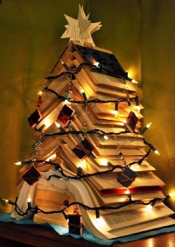 Árvore de Natal criado com livros empilhados e decoração com pisca-piscas, penduricalhos em formato de livros e uma estrela feita a partir da página dos livros.