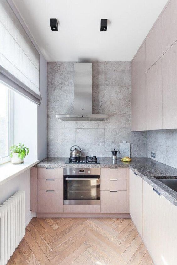 Cozinha planejado em "L" com armários rosas, bancada e revestimento em cinza e chão em madeira.