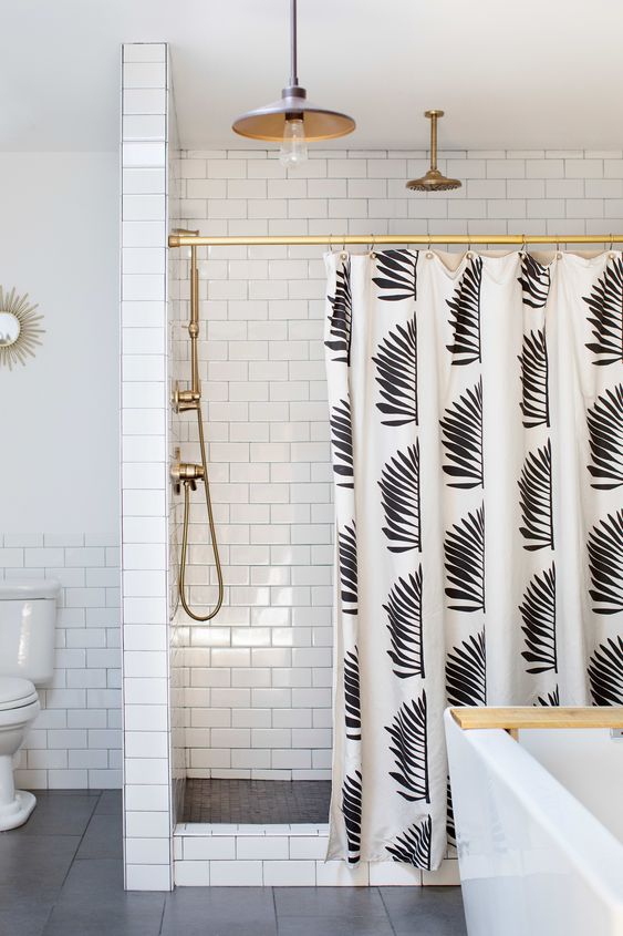 Banheiro com azulejos brancos, metais dourados e cortina para banheiro com branca com estampa de folhas pretas.