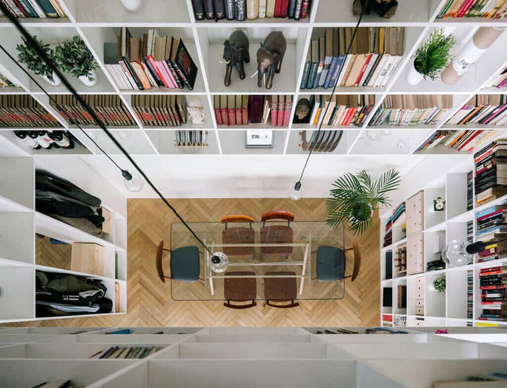 Fotografia tirada de cima para baixo de uma biblioteca em casa. O pé-direito ampliado possibilitou a criação de muitos espaços para livros.