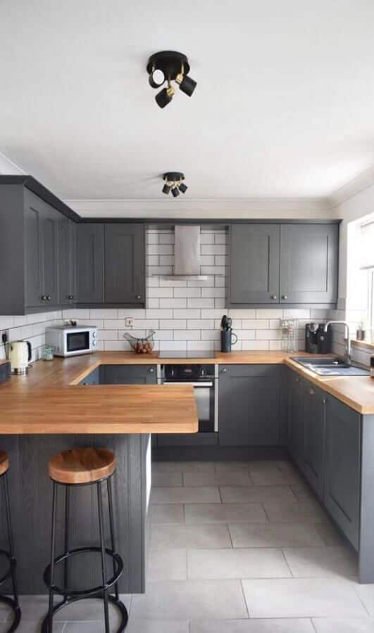 Cozinha com armários cinzas, azulejos brancos e bancada em madeira.