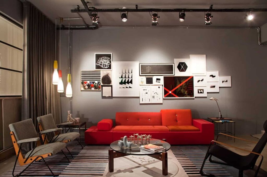 Decoração despojada e moderna feita com trilho de iluminação e alguns pendentes, num ambiente que possui cadeiras modernas, quadros em preto e branco e um sofá vermelho vibrante.