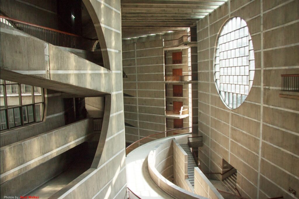O interior do edifício brutalista deixa a materialidade aparente. A iluminação valoriza a estética.