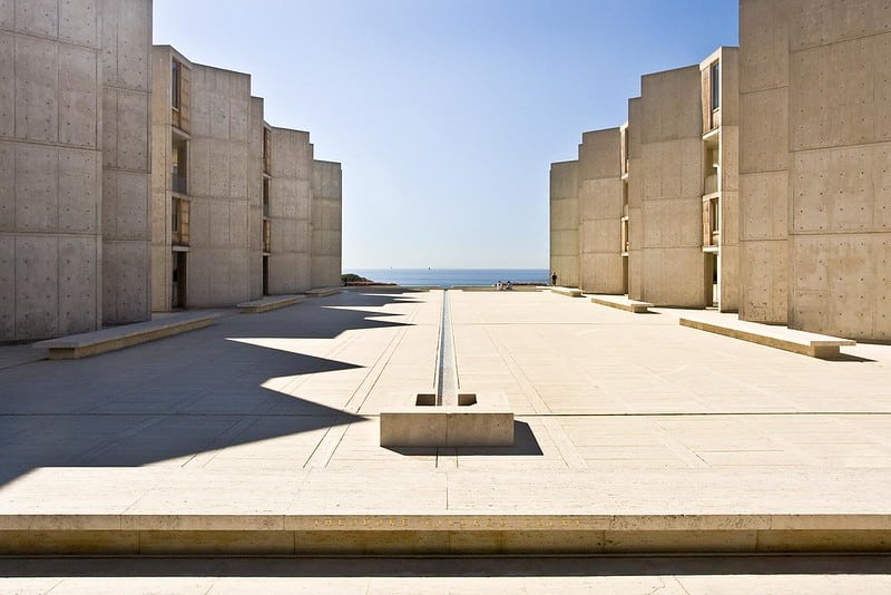 Dois conjuntos de edifícios com materiais em placas de cimentícias. Ao centro, um grande pátio deixa a vista livre para o mar.