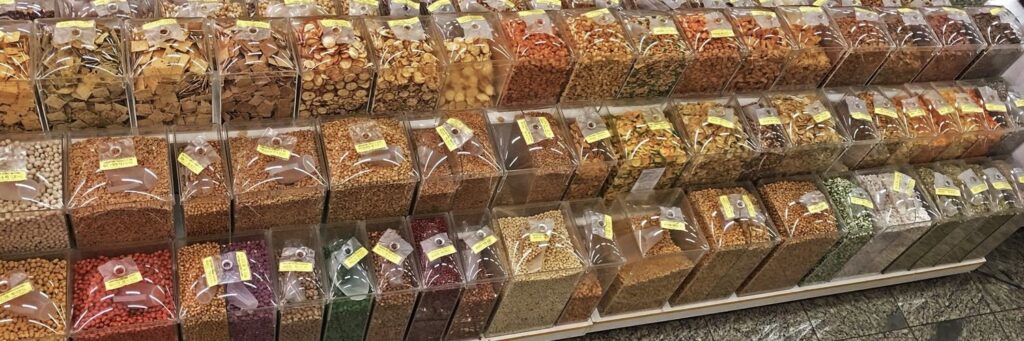 Expositor de uma típica loja da Zona Cerealista, com variedade de produtos incluindo grãos, frutas secas, ervas, temperos e mais.