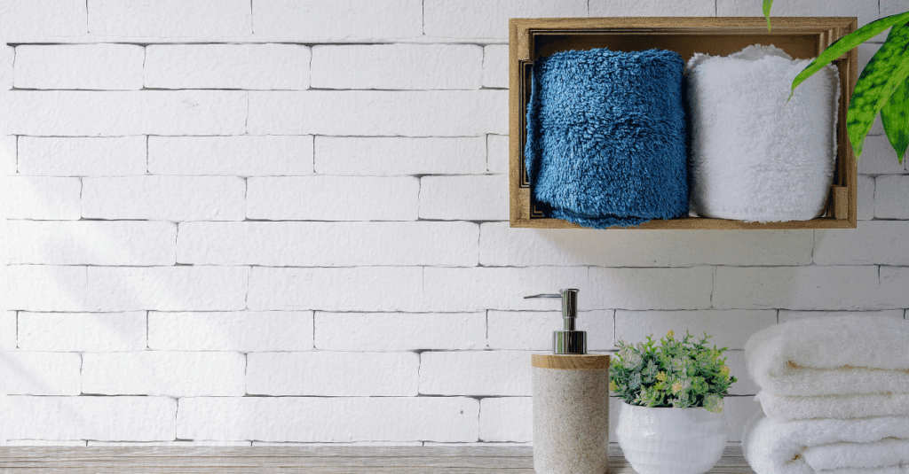 Parede com revestimento que imita tijolos brancos, com decoração com plantas e toalhas brancas e azul.
