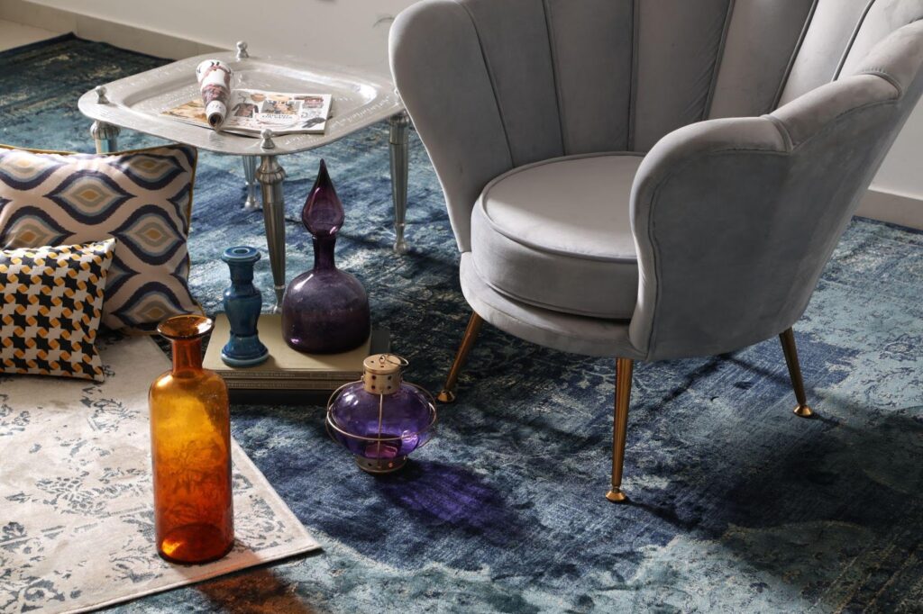 Sala decorada com poltrona cinza, vasos coloridos e um tapete azul com diferentes tons.