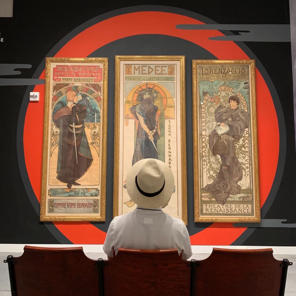 Três cartazes emoldurados sendo que, ao centro, é retratada a atriz Sarah Bernhardt.