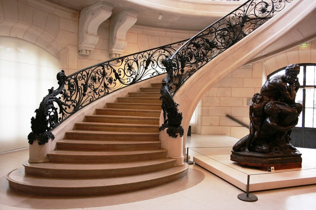 Escadas com corrimãos esculturais em metal retorcido, relembrando a temática de flores e folhas, típica do Art Nouveau.