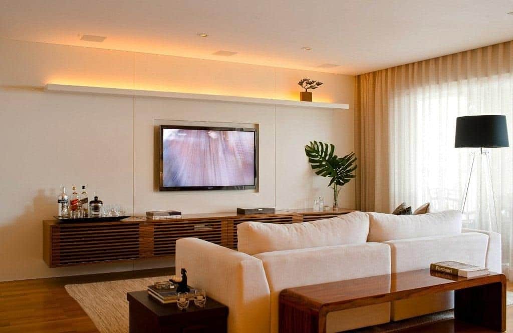 Sala decorada com televisão acoplada na parede e plafons utilizados na iluminação do cômodo.