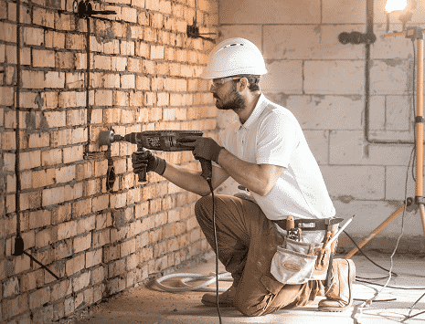 Quanto custa preparar um imóvel pronto para morar? - Homem no processo de instalação elétrica, utilizando uma ferramenta na parede.