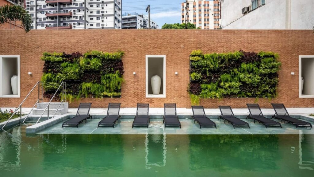 Vista da piscina com deck molhado. Ao fundo, uma parede com vasos decorativos e jardim vertical.