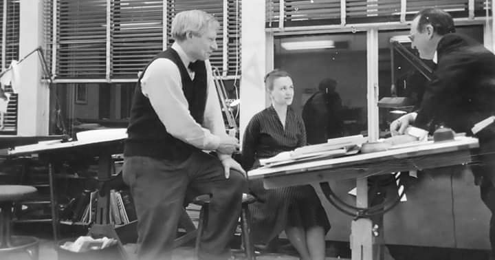 Louis Kahn conversando com Anne e um homem, em seu escritório. Todos estão em volta de uma prancheta com desenho.