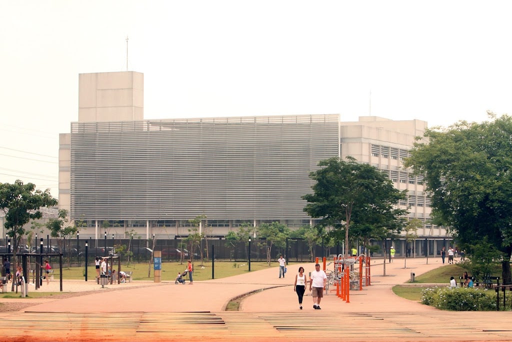 Na Área Institucional é possível ver a Biblioteca de São Paulo e alguns espaços reservados para caminhada, onde pessoas transitam em meios às arvores.