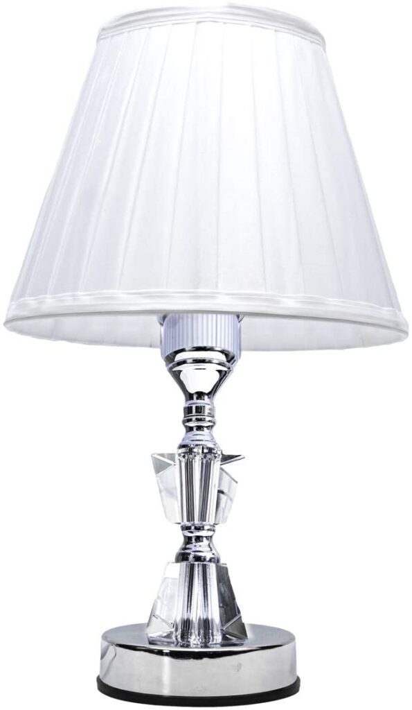 Tipos de luminárias: abajur, em uma mesinha branca, ao lado de outros objetos.