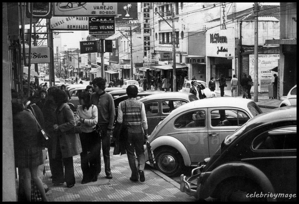 Na década de 1970, a rua Augusta já contava com muitas lojas e restaurantes. Pessoas andam pelas calçadas e os carros (Fuscas) estão estacionados. 