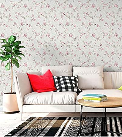 Papel de parede floral numa sala decorada com plantas, sofá, mesinha de centro com livros e almofadas coloridas (xadrez e vermelho).