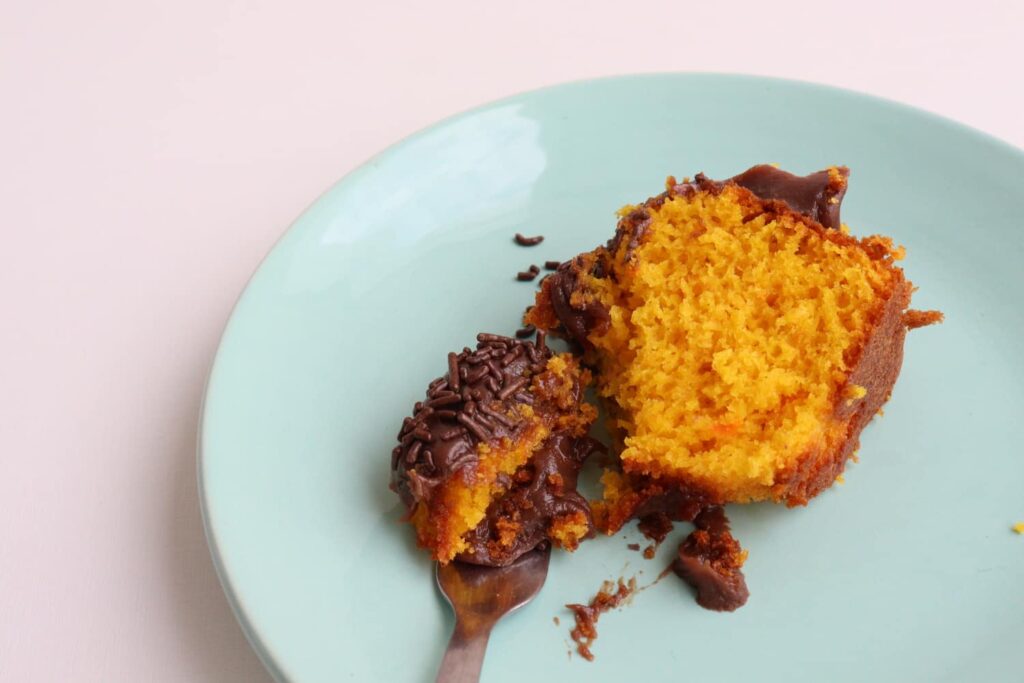 Pedaço de bolo de cenoura fofinho com cobertura de brigadeiro, sobre um prato azul claro.