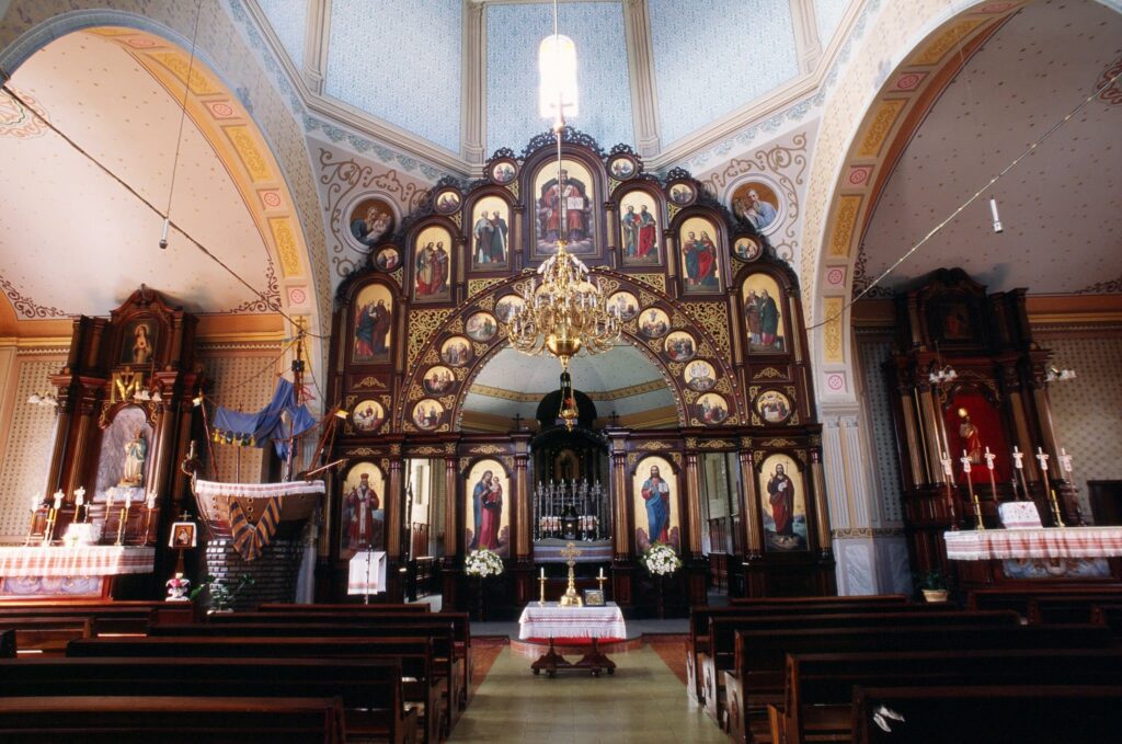 Fotografia do interior da igreja com traços bizantinos, com amplo painel em madeira ornamentado.