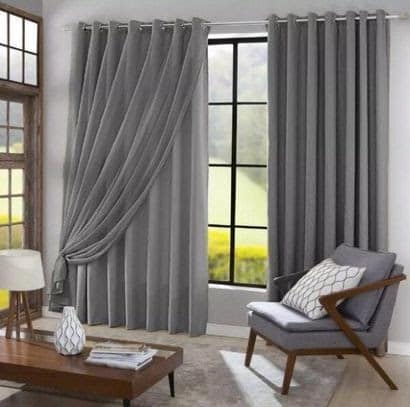 Sala de estar em tons de cinza, com uma cortina grande na mesma cor. As cortinas funcionam como pequenos reparos que corrigem a incidência de luz nos ambientes.