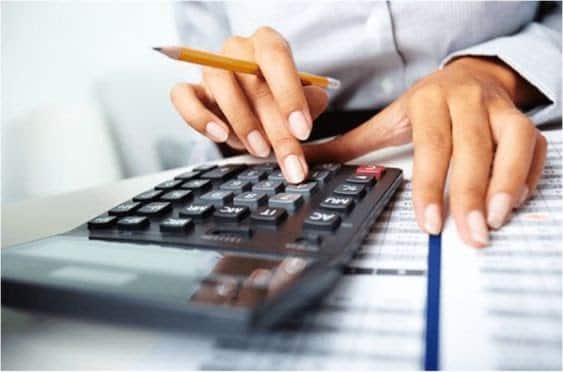 Pessoa fazendo cálculos em uma calculadora. enquanto segura um lápis, representando como é possível  usar o home equity para pagar a faculdade dos filhos