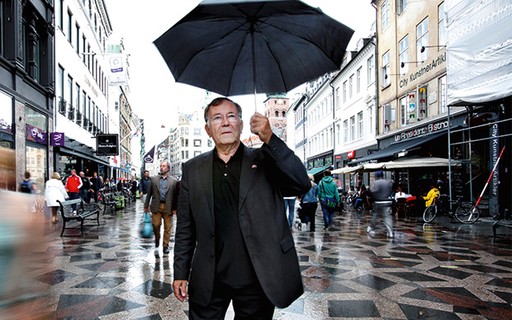 Jan Gehl no meio da rua com uma roupa preta e um guarda chuva preto.
