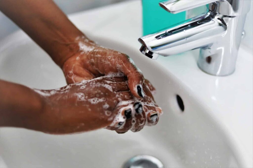 Pessoa ensaboando as mãos com a torneira fechada.